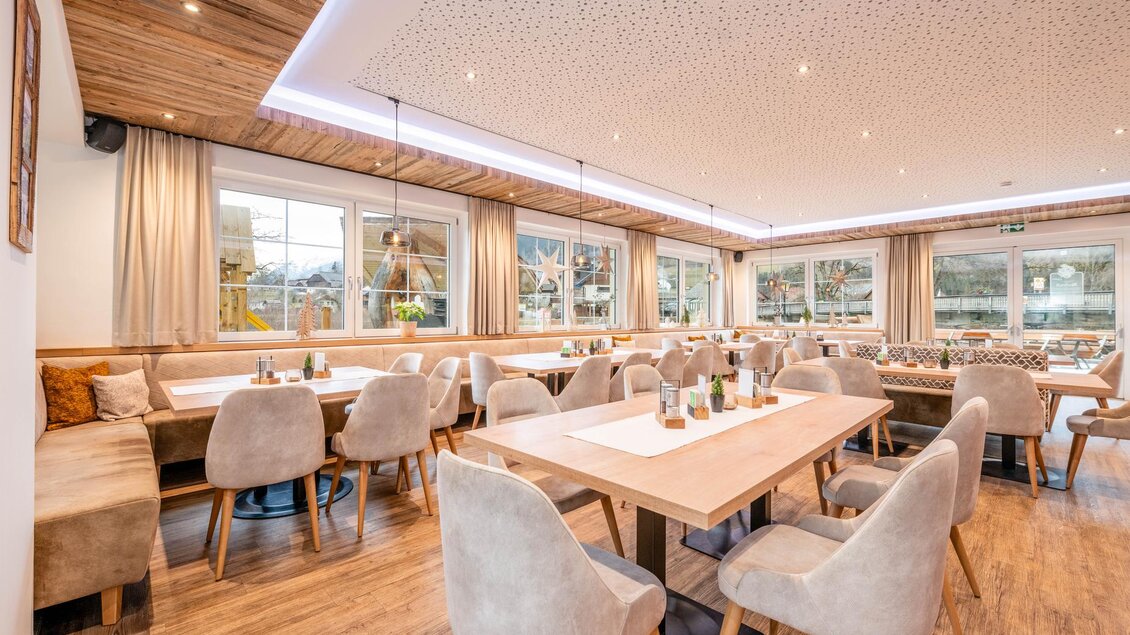 Ein modernes Restaurant mit warmem Holzdekor und gemütlichen Sitzgelegenheiten. Große Fenster sorgen für viel Tageslicht und bieten einen Blick nach draußen.