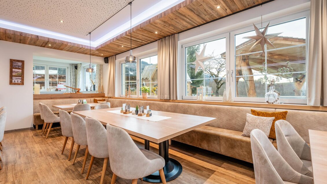 Ein modernes Restaurant mit holzverkleideten Decken und gemütlichen Sitzgelegenheiten. Die großen Fenster bieten einen Blick auf die Außenanlage und sorgen für viel Tageslicht.