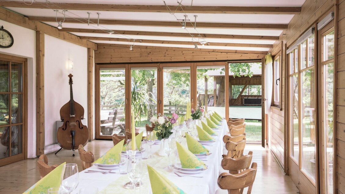 Heller Gastraum im Landhof Lazarus in Mooskirchen mit gedeckter Tafel, Holzstühlen und großen Fenstern zum Garten | © LazarusSoulbrand
