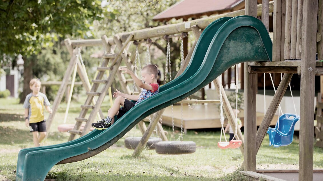 Zwei Kinder spielen auf einem Spielplatz mit Rutsche, Schaukel und Holzklettergerüst beim Landhof Lazarus in Mooskirchen | © LazarusSoulbrand