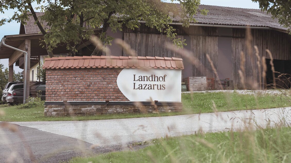 Zufahrt zum Landhof Lazarus in Mooskirchen mit Namensschild an einer Mauer, Wirtschaftsgebäude und Bäumen im Hintergrund | © LazarusSoulbrand