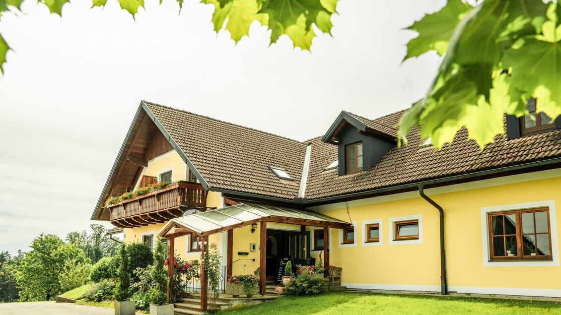 Landhof Lazarus in Mooskirchen mit gelber Fassade, Holzbalkon, überdachtem Eingang und Garten | © Region Graz - Mias Photoart