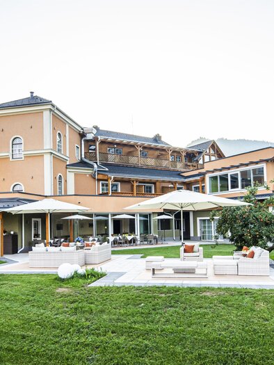 Ein elegantes Hotelgebäude umgeben von einer grünen Wiese und Bergen. Die Terrasse lädt zum Entspannen im Freien ein. | © Landhotel Timmerer