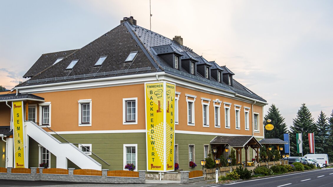 Einfarbiges Gebäude mit orangefarbenen und grünen Wänden. Vor dem Gebäude befinden sich eine Treppe und ein Eingangsbereich mit Terrasse. | © Landhotel Timmerer
