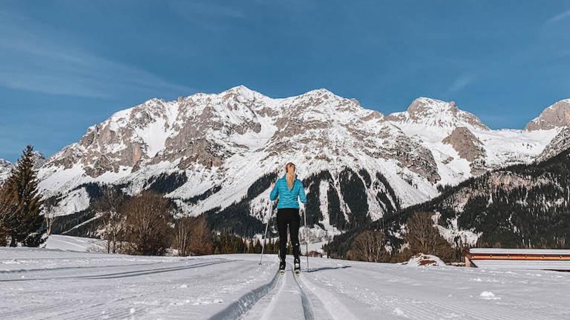 Eine Person läuft auf einer schneebedeckten Strecke in den Bergen. Der Himmel ist klar und blau, umgeben von beeindruckenden Bergriesen. | © Nina Zasche