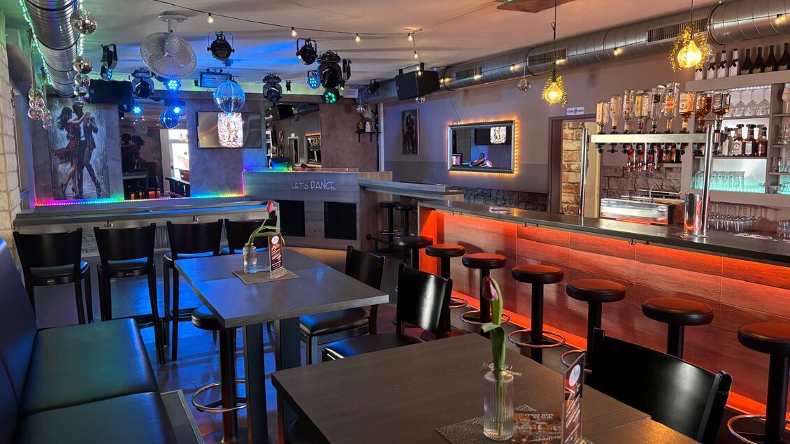 Eine stylische Bar mit modernen Sitzplätzen und bunten Lichtern. Der Raum scheint einladend für gesellige Abende zu sein. | © Let's Dance/Rainer Kohlhauser