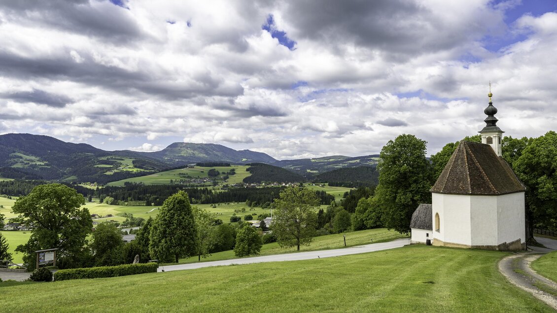 Eine kleine Kirche auf einer Wiese, umgeben von Bäumen. Der Himmel ist bewölkt mit einigen Sonnenstrahlen. | © Tourismusverband Oststeiermark