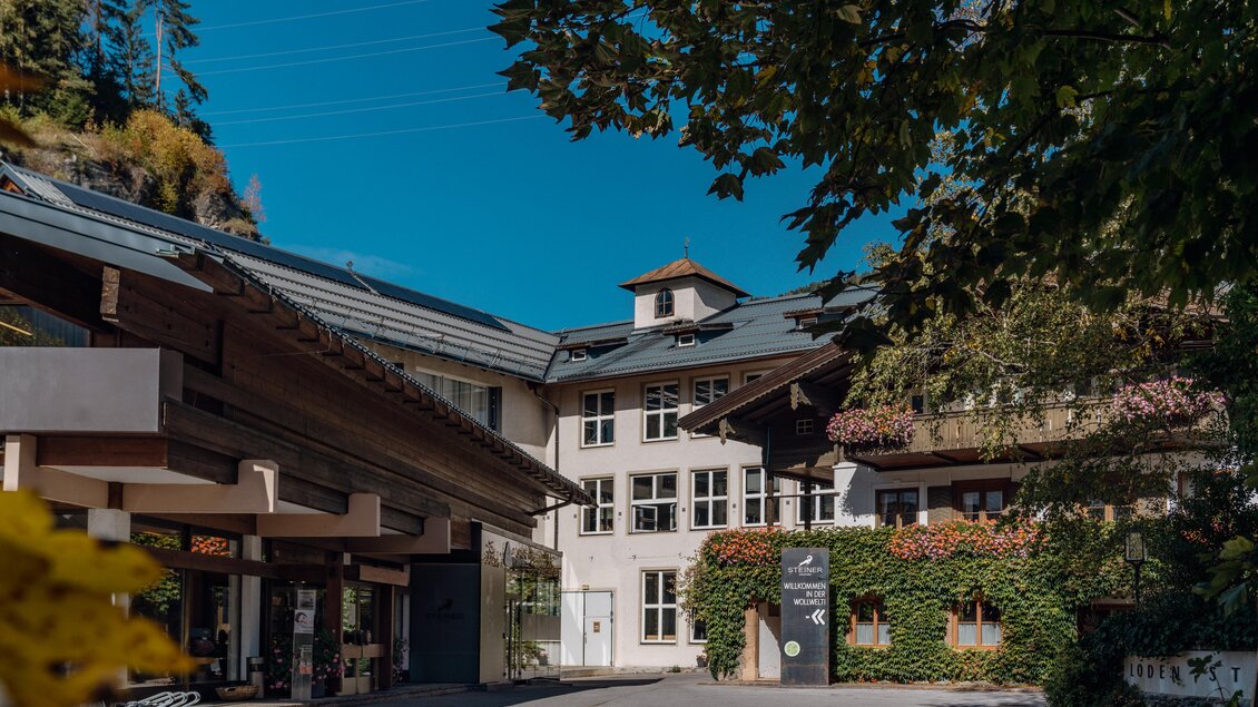 Ein attraktives Gebäude mit moderner Architektur und grüner Bepflanzung. Im Hintergrund ist ein blauer Himmel sichtbar. | © Lodenmanufaktur Steiner1888 | Fotografin Christine Höflehner
