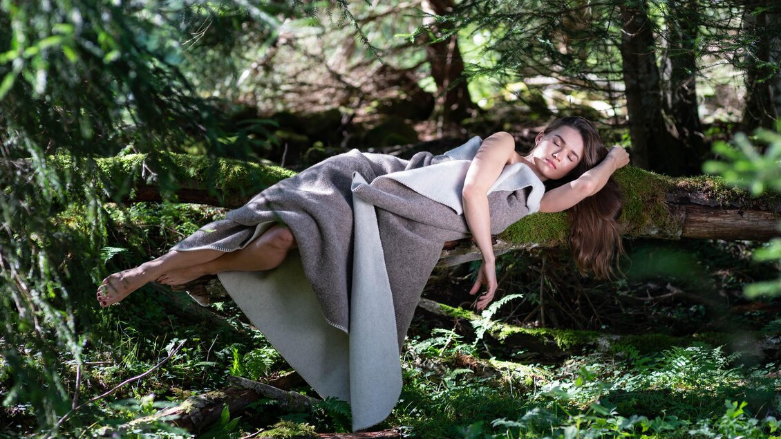 Eine Frau schwebt entspannt in einem Wald auf einem Baumstamm. Die Umgebung ist grün und umgeben von Bäumen. | © © 2022 Andreas Pilz - KARAKORUM