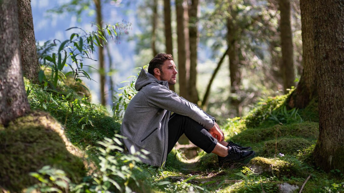 Ein Mann sitzt auf dem Boden im Wald, umgeben von grünen Pflanzen und Bäumen. Die Lichtverhältnisse schaffen eine ruhige und entspannte Atmosphäre. | © © 2022 Andreas Pilz - KARAKORUM