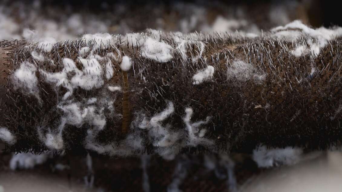Eine Nahaufnahme von braunem Stoff mit weißen Fusseln darauf. Der Hintergrund zeigt verschwommene Details, die eine warme und gemütliche Atmosphäre vermitteln. | © © 2021 Alwin Strasser - strasserconcept