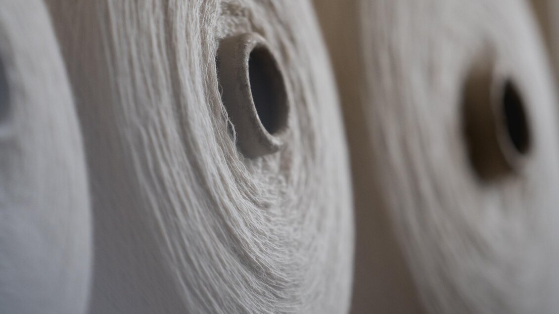 Eine Reihe von Spulen mit weißem Garn. Die Spulen sind ordentlich aufgereiht und zeigen die Textur des Materials. | © © 2021 Alwin Strasser - strasserconcept