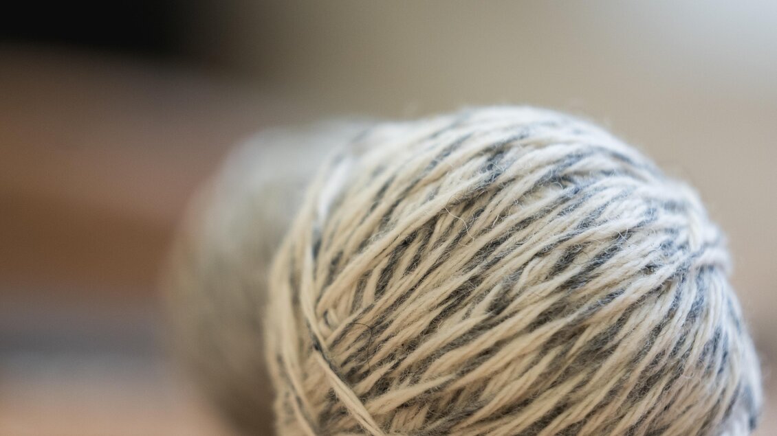 Ein grauer Wollball liegt auf einem Holztisch. Die mit Licht durchflutete Umgebung schafft eine warme Atmosphäre. | © © 2021 Alwin Strasser - strasserconcept