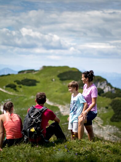 Auf dem Losergipfel genießt eine Familie die Aussicht auf die umliegende Berglandschaft des Ausseerland Salzkammerguts unter blauem Himmel. | © TVB Ausseerland-Salzkammergut/Tom Lamm
