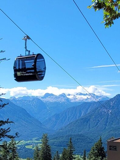 Eine Seilbahn schwebt über die Berge mit einer Aussicht auf grüne Täler und hohe Gipfel. Der Himmel ist klar und sonnig. | © Rudolf Gasperl