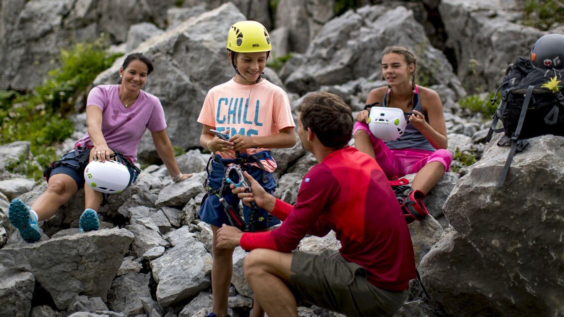 <p>Eine Gruppe von vier Personen bereitet sich auf das Klettern am Loser vor. Sie sitzen in der felsigen Landschaft am Berg in Altaussee und hören den Erklärungen gespannt zu.</p> | © TVB Ausseerland - Salzkammergut-Tom Lamm