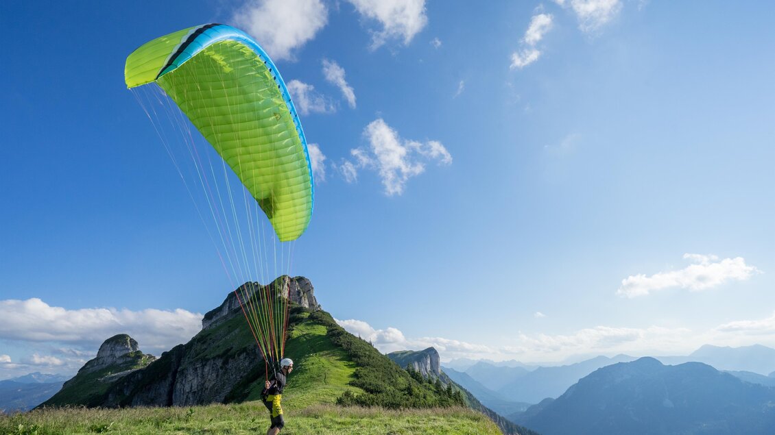 <p>Ein Paragleiter steht auf einer grünen Wiese am Loser und bereitet sich zum Abflug vor. Im Hintergrund sind beeindruckende Berggipfel des Ausseerlandes und ein blauer Himmel zu sehen.</p> | © Loser Bergbahnen Altaussee/F. Loitzl