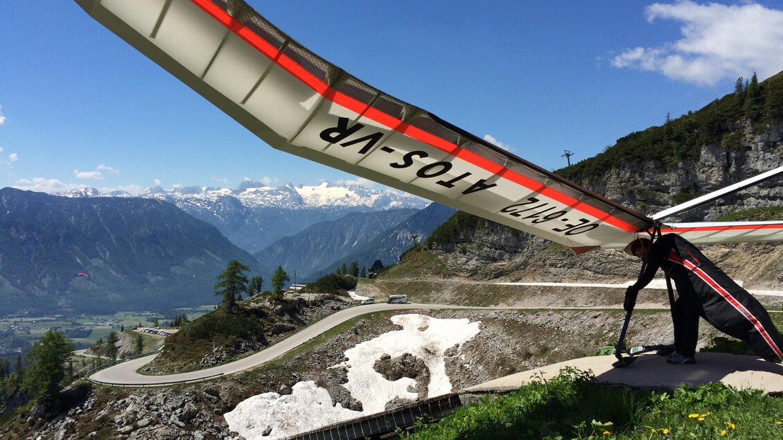 <p>Ein Drachenflieger bereitet sich auf den Abflug vom Loser hinunter vor. Im Hintergrund liegt sogar noch ein wenig Schnee auf dem Loser und eine freie Sicht auf den Dachstein ist möglich.</p> | © Loser Bergbahnen/M. Raich