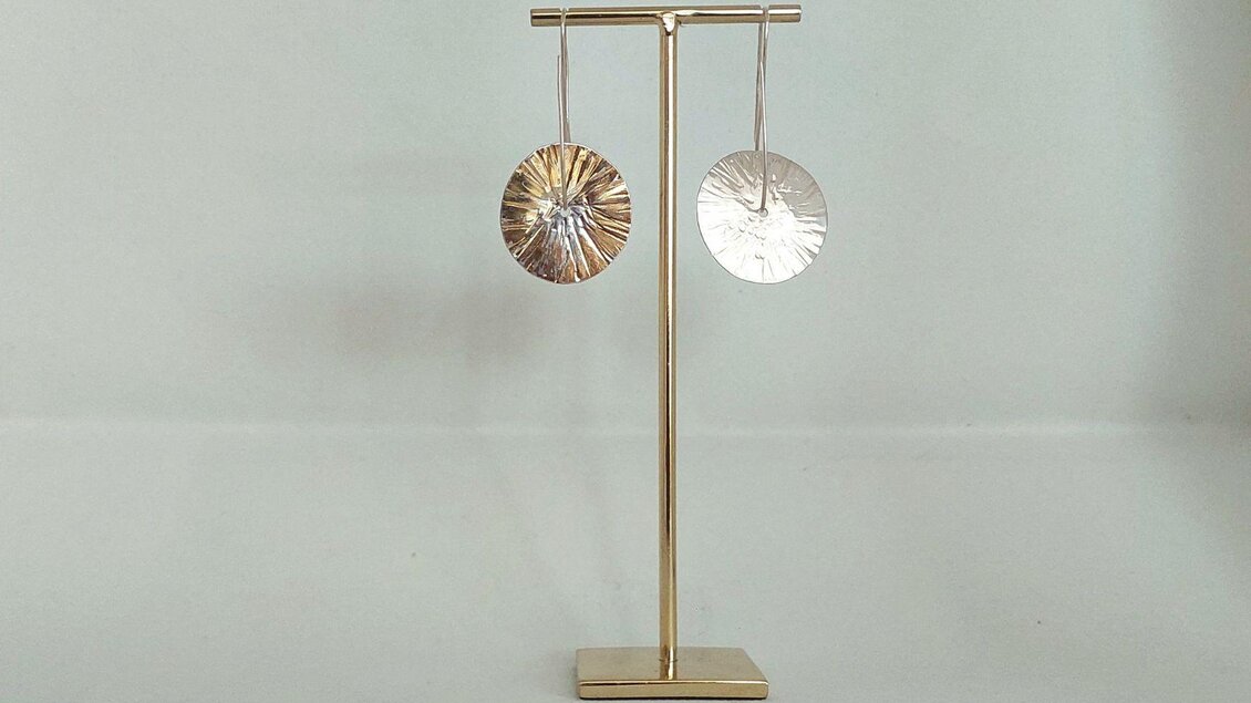 Eine Nahaufnahme eines Ohrringpaars in Form eines Kreises aus Gold beidseitig tragbar, präsentiert auf einem goldenen Ständer. | © Lisa Wagenhofer