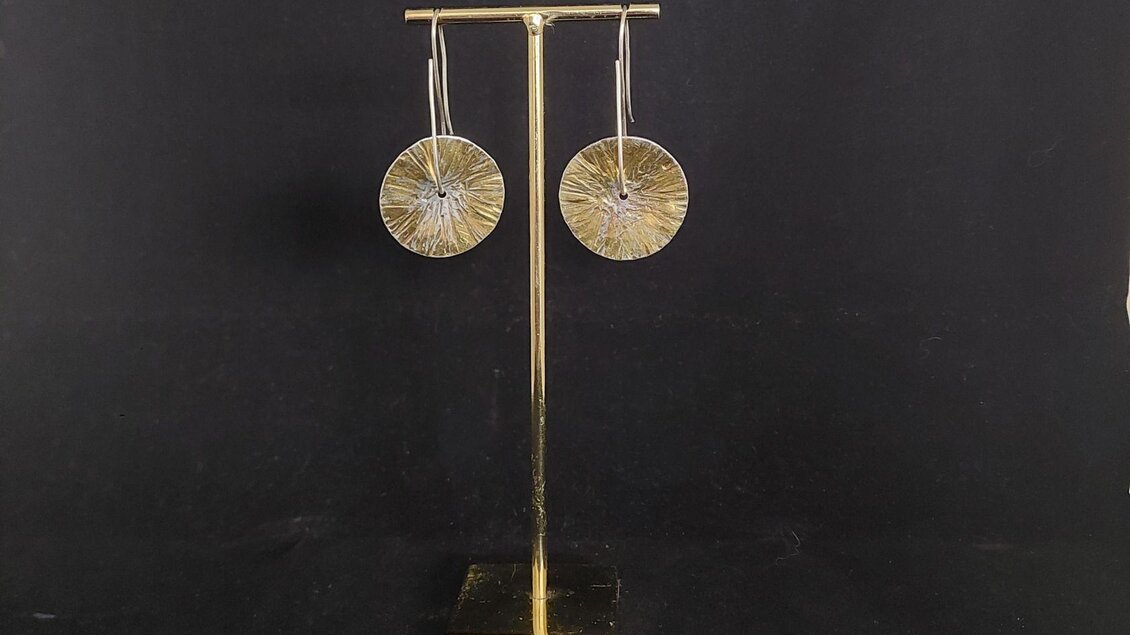 Eine Nahaufnahme eines Ohrringpaars in Form eines Kreises aus Gold beidseitig tragbar, präsentiert auf einem goldenen Ständer. | © Lisa Wagenhofer
