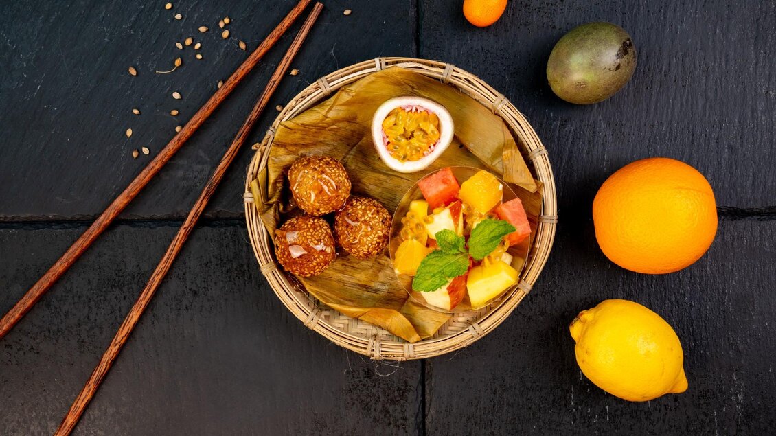Sesambällchen und exotischer Obstsalat mit Passionsfrucht und Minze im Bambusteller. | © Má Kitchen