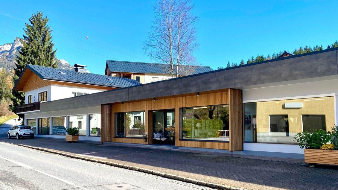 <p>Das Gebäude vom Möbel Peer in Bad Aussee mit Holz- und Glasdetails. Die Straße vor dem Gebäude ist gut zugänglich und von Bäumen umgeben.</p> | © Möbel Peer_Sabine Stöckl