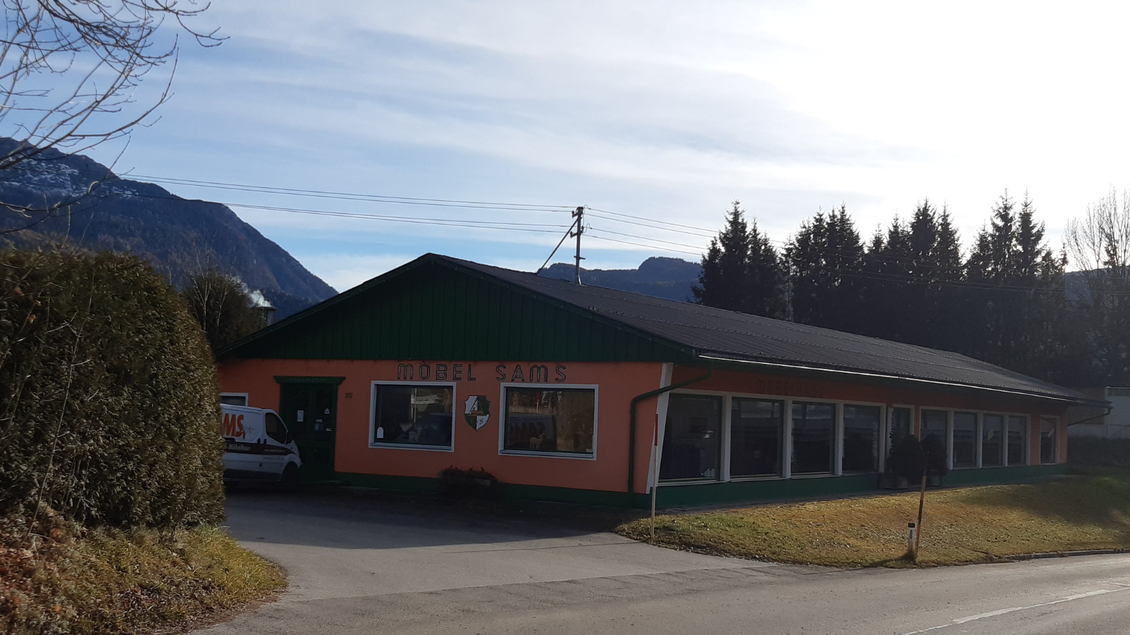 Ein Möbelgeschäft mit orangefarbenem und grünem Außenanstrich. Im Hintergrund sind Berge und ein klarer Himmel sichtbar. | © TVB Ausseerland Salzkammergut_Daniela Casari