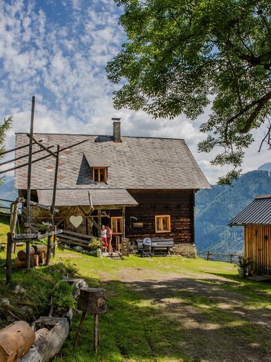 A picturesque mountain cabin surrounded by trees and a beautiful landscape. The sky is clear, and the atmosphere is calm and inviting. | © Manfred Müller