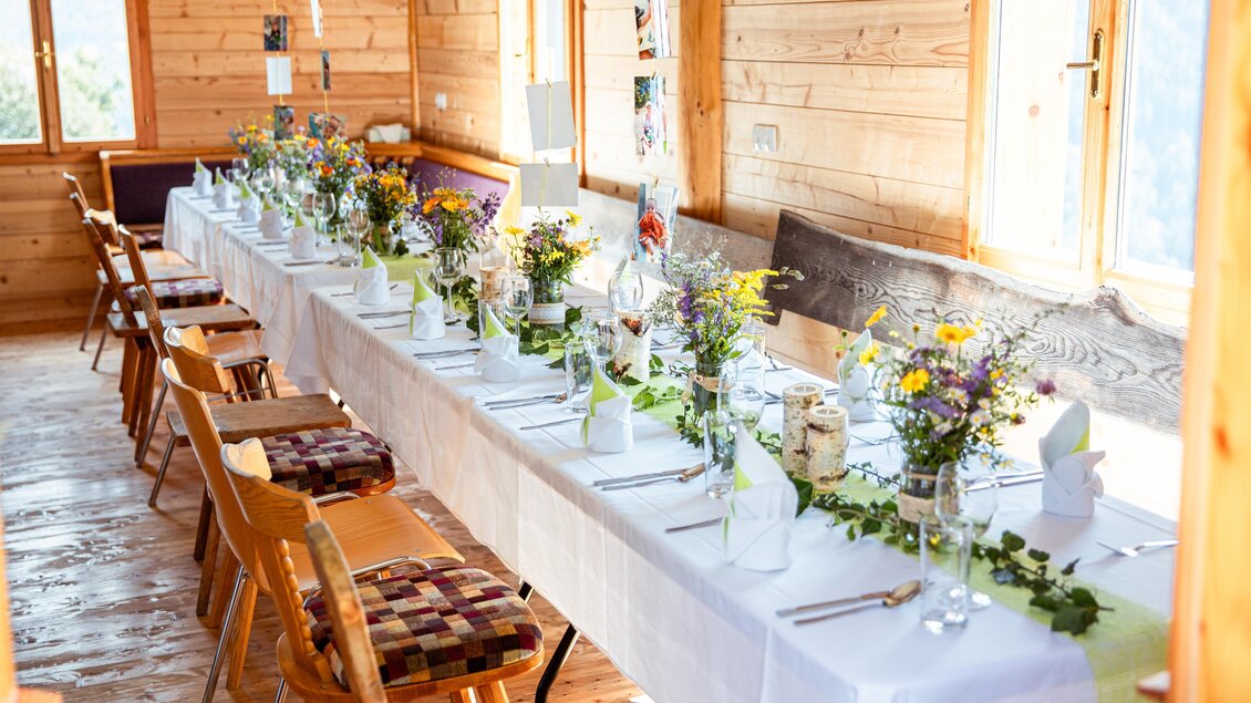 Ein schön gedeckter Tisch mit bunten Blumenarrangements in einem Holzraum. Die Sonne scheint durch die Fenster und schafft eine einladende Atmosphäre. | © Manfred Müller
