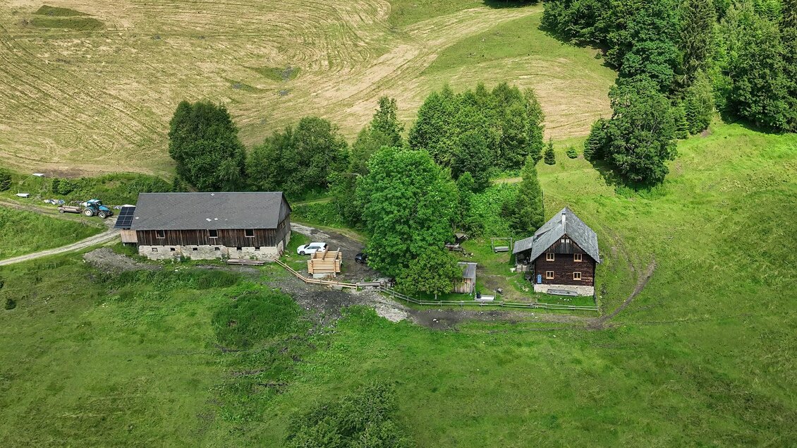 Eine ruhige ländliche Landschaft mit zwei Gebäuden und umgeben von grünen Wiesen und Bäumen. Im Hintergrund sind Felder zu sehen. | © Müller