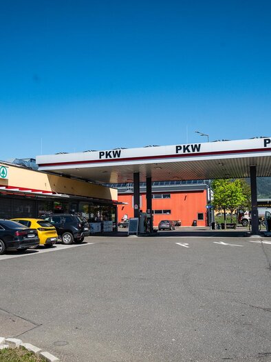Eine Tankstelle mit mehreren Fahrzeugen davor und einem Supermarkt in der Nähe. Der Himmel ist klar und blau. | © M-Rast