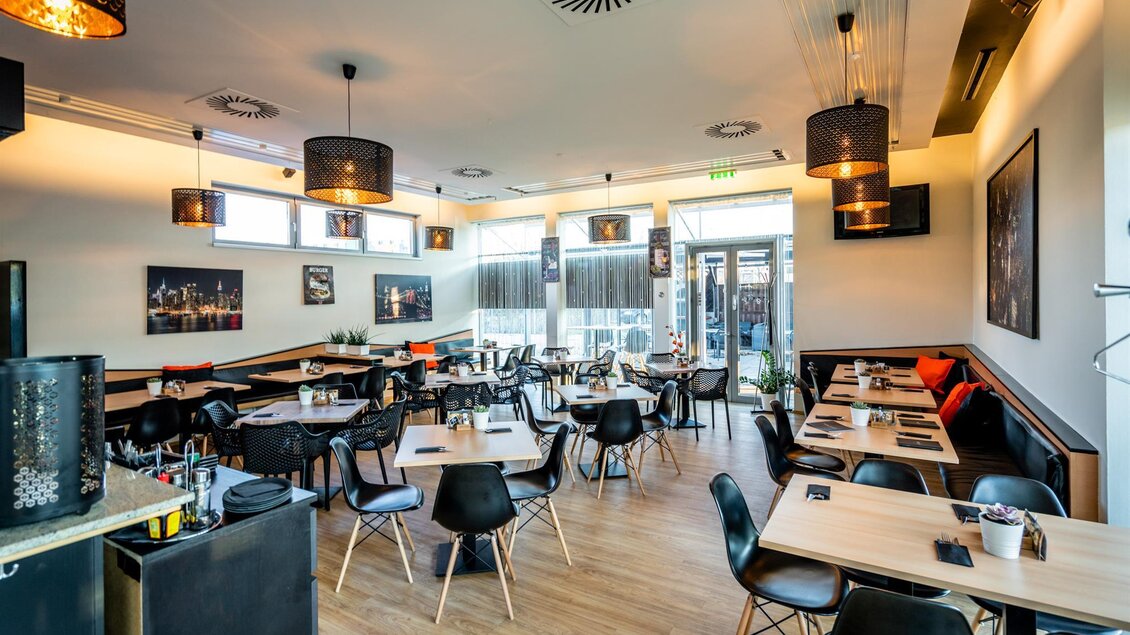 Ein modernes Restaurant mit eleganten Tischen und Stühlen. Die Atmosphäre ist hell und einladend, mit großen Fenstern und stilvollen Lampen. | © Stephan Friesinger