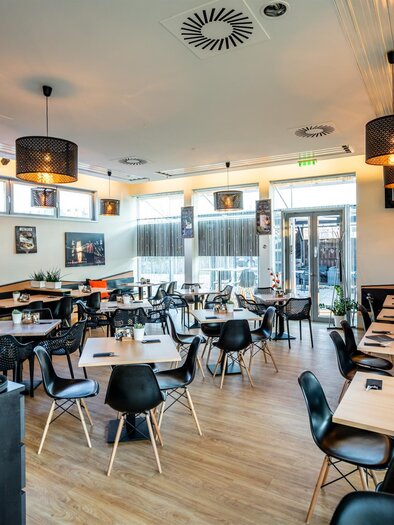 Ein modernes Restaurant mit eleganten Tischen und Stühlen. Die Atmosphäre ist hell und einladend, mit großen Fenstern und stilvollen Lampen. | © Stephan Friesinger