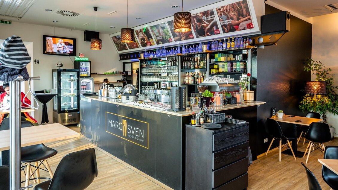Eine moderne Bar mit einem eleganten Tresen und Holzfußboden. An der Wand sind Bilder und eine gut sortierte Getränkeauswahl zu sehen. | © Stephan Friesinger