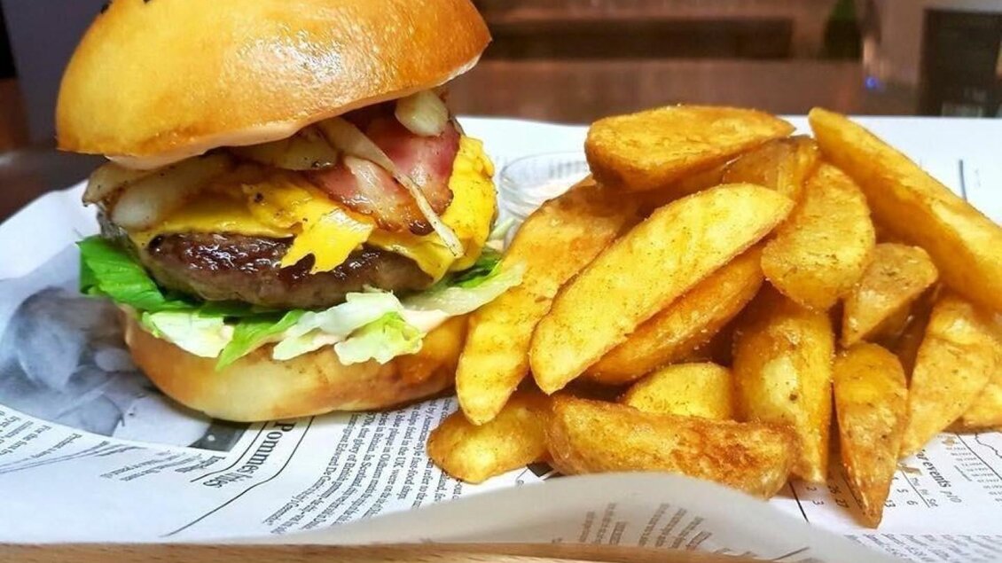 Ein saftiger Burger mit Käse, Speck und frischem Gemüse, serviert auf einem Brötchen. Dazu gibt es knusprige Kartoffelecken. | © Stephan Friesinger