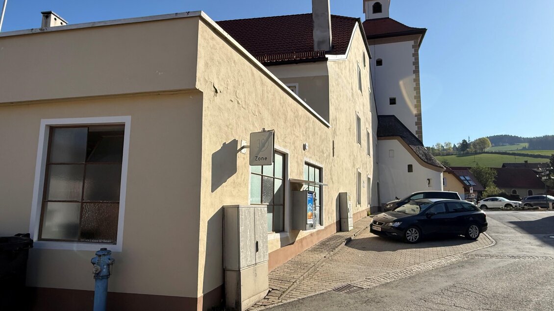 Ein Gebäudekomplex mit hellen Wänden und einem Turm im Hintergrund. Es stehen einige Autos auf der Straße in einer ruhigen Umgebung. | © Markus Kaltenegger
