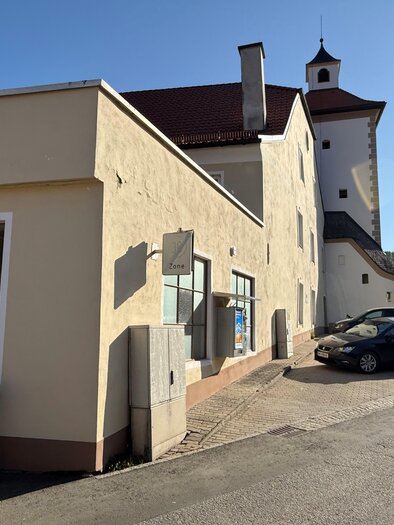 Ein Gebäudekomplex mit hellen Wänden und einem Turm im Hintergrund. Es stehen einige Autos auf der Straße in einer ruhigen Umgebung. | © Markus Kaltenegger