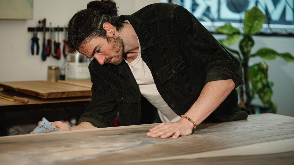 Manuel Stangl schleift mit einem Schleifklotz eine große Holzplatte im MORI Atelier. | © Bernd Grosseck