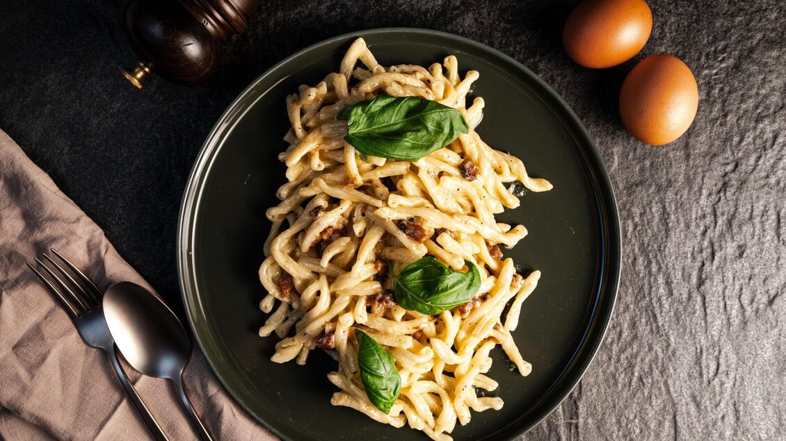 Ein Teller mit Pasta, garniert mit frischem Basilikum. Daneben liegen zwei Eier und eine Gewürzmühle. | © Mundus kitchen