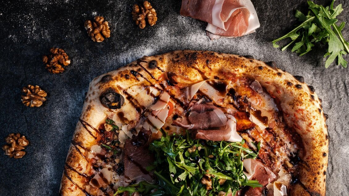 Eine köstliche Pizza mit Schinken, Rucola und Nüssen. Der rustikale Teig ist perfekt knusprig und gut garniert. | © Mundus kitchen