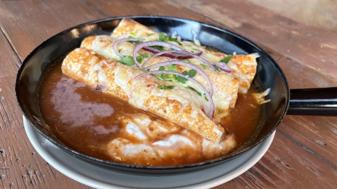 Ein Gericht mit Enchiladas in einer scharfen Sauce, garniert mit Zwiebeln und Koriander. Serviert in einer kleinen Pfanne auf einem Tisch aus Holz. | © Stadtmarketing Judenburg
