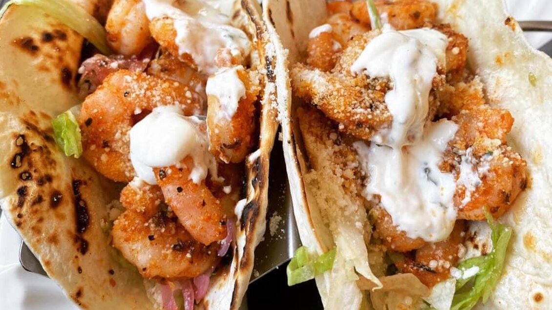 Zwei köstliche Garnelen-Tacos auf einem Teller. Sie sind mit frischem Gemüse und einer cremigen Sauce garniert. | © Mamas Tacos