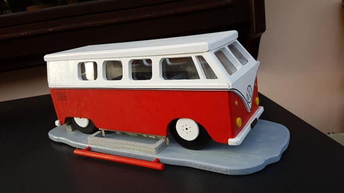 Ein roter und weißer Spielzeug-Bus im Vintage-Stil steht auf einem Tisch. Das Modell zeigt die charakteristische Form eines klassischen VW-Busses. | © Oskar Stieg
