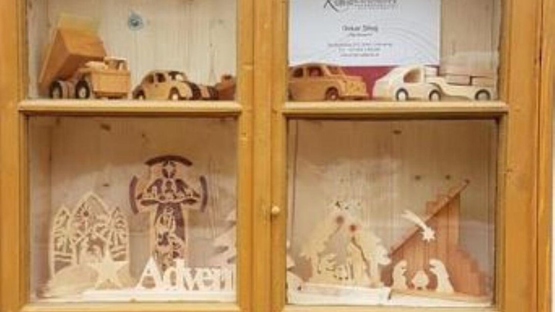 Eine Vitrine mit Holzspielzeugen und handgefertigten Figuren. Die Auslage zeigt verschiedene Motive, darunter Autos und Bauwerke. | © Oskar Stieg