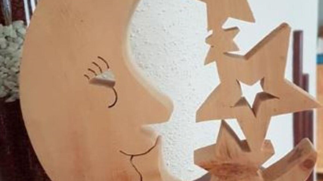 Eine hölzerne Skulptur in Form eines Mondes mit einem lächelnden Gesicht und zwei Sternen. Die Statue steht auf einem kleinen, quadratischen Sockel. | © Oskar Stieg