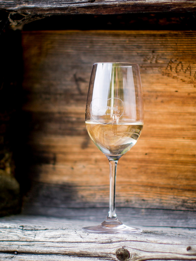 Ein elegantes Weinglas steht vor einer rustikalen Holzoberfläche. Der Wein im Glas reflektiert das Licht wunderschön. | © TVB_ Ausseerland Salzkammergut_Tom Lamm