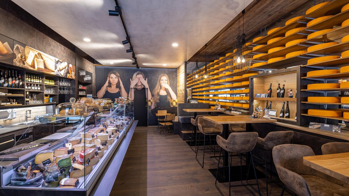 Ein modernes Café mit rustikaler Einrichtung und ansprechenden Holzregalen. Es bietet eine große Auswahl an Käse und Getränken in einem einladenden Ambiente.