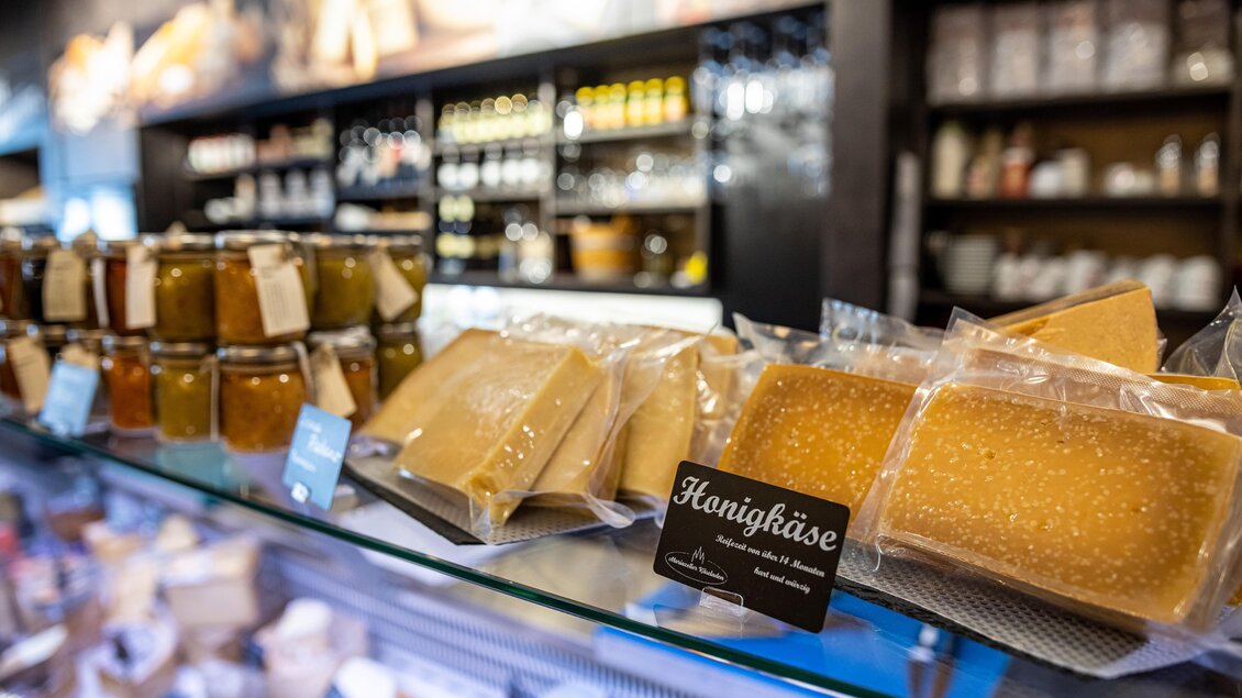 Eine Vielfalt an Honigkäse und Marmelade auf einem Regal. Die Produkte sind ordentlich in Gläsern und Verpackungen angeordnet.