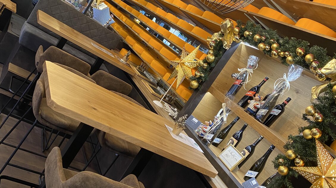 Ein modernes Restaurant mit Holzstühlen und einem langen Tisch. Die Wände sind mit warmen Farben und festlichen Dekorationen geschmückt.
