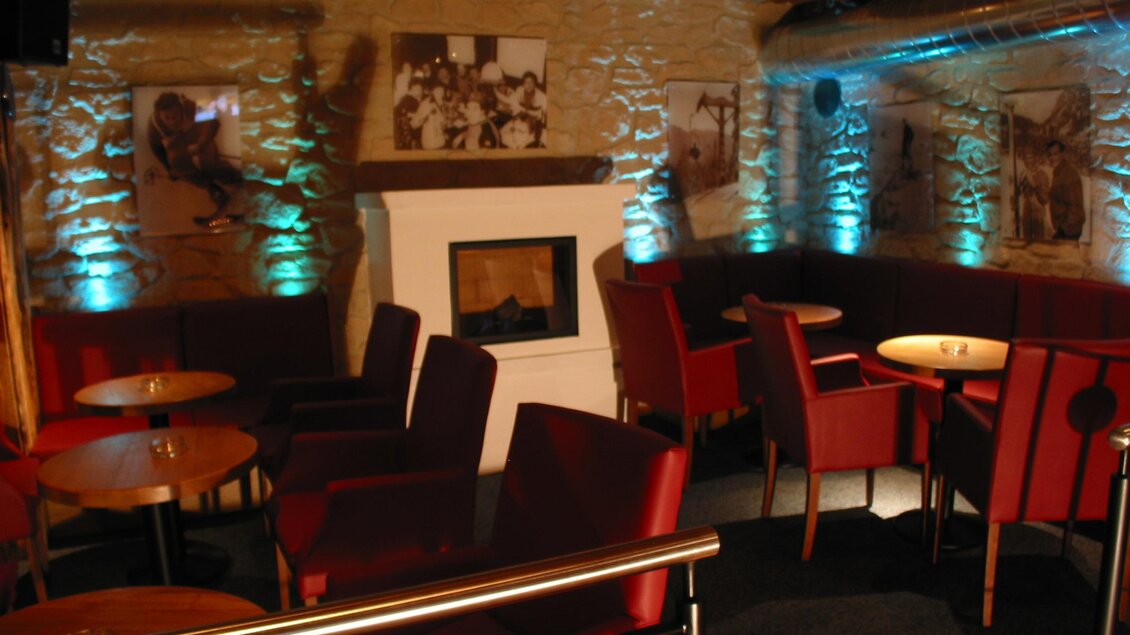 Marios Pizzeria Sportalm Tauplitz Eine gemütliche Lounge mit roten Sesseln und Holztischen. An den Wänden sind historische Fotos und eine Kaminecke zu sehen. | © Mario Seebacher